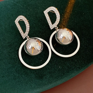 Detailed view of silver hoop earrings with pave letter D and sphere charms on green velvet