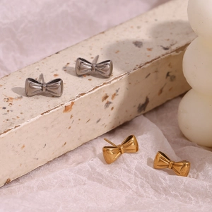 Detail of minimalist bow-shaped earrings in gold and silver finish on textured stone