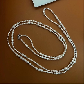 Macro shot of layered white freshwater pearl necklace with silver metal clasp on brown base