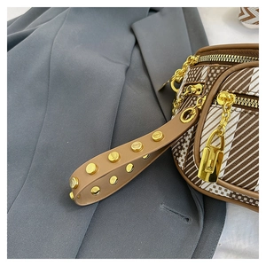 Detail of geometric stripe saddle bag featuring gold rivets on strap and metal zipper