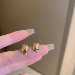 Gold plated minimalist metal bean stud earrings held by hand to show compact size