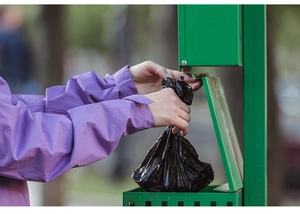 Detail of hand pulling black biodegradable dog poop bag from dispenser in a park setting