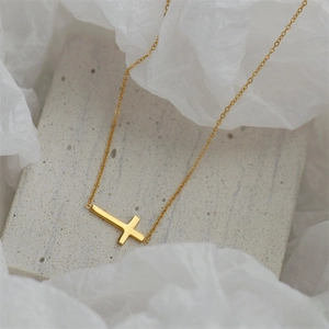 Detailed macro view of a side-set gold cross necklace on a minimalist stone surface