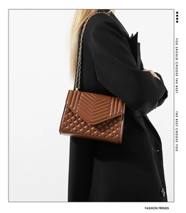 Detail of a brown quilted leather crossbody bag with V-pattern and gold chain strap