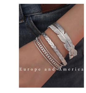 Close-up of a 4-piece silver bracelet set featuring feather and chain designs on denim