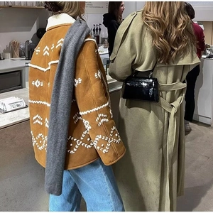 Detail shot of brown lambswool jacket with white geometric embroidery in cafe setting