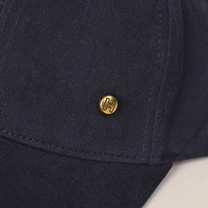 Detailed close-up of the navy cotton twill fabric and gold metal H-letter emblem