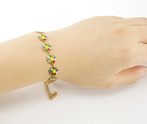 Detail of 18K gold stainless steel bracelet with colorful daisy charms on a female wrist
