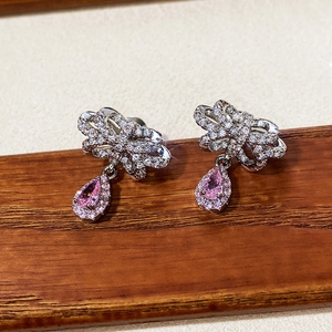 Detail of pink pear-shaped gemstone earrings with sparkling bow accent on wood stand
