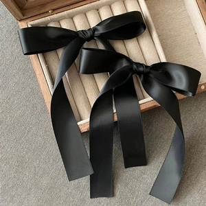 Detailed view of two black satin ribbon bow hair clips on a wooden jewelry display box