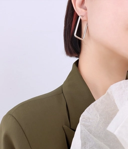 Close-up of minimalist silver rectangular earrings worn by a model in bright light