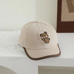 Close-up of beige canvas kid baseball cap featuring a cute brown bear embroidery patch
