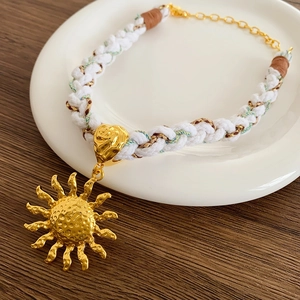 Close-up of golden sun pendant with hammered texture on white woven rope necklace