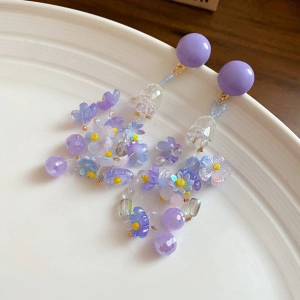 Détail de boucles d'oreilles fleurs mauves avec perles sur une plaque céramique