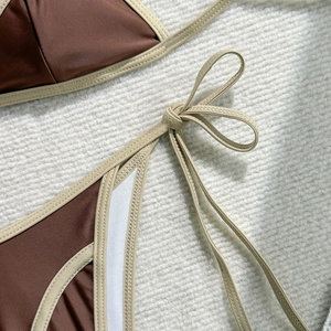 Close-up detail of smooth brown bikini fabric with beige side-tie knot and precise stitching