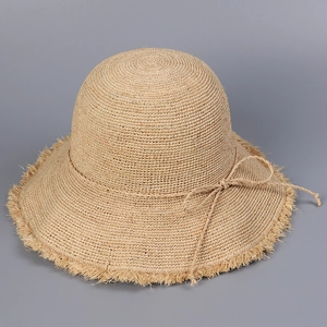 Close-up of handmade raffia sun hat with woven texture, fringed edge and straw bow
