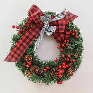 Christmas wreath with buffalo plaid bow, red berries and pine cones on grey background