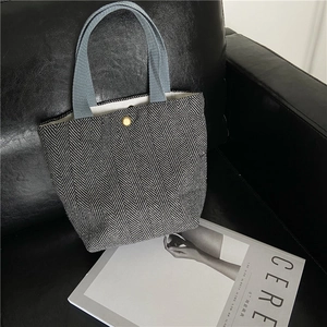 Detail of herringbone wool fabric handbag featuring a blue strap and gold magnetic clasp