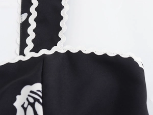 Detail des geblümten Ausschnitts mit weißem Wellensaum an einem schwarzen ärmellosen Kleid
