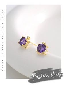 Macro detail of gold turtle earrings with purple cubic zirconia on a white surface