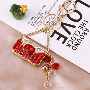 Macro shot of gold envelope-shaped bag keychain with red crystals on champagne silk