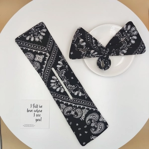 Detail of black paisley fabric bun maker and matching bow headband on a white table