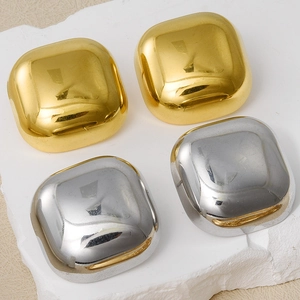 Macro detail of glossy square geometric stud earrings in gold and silver on stone