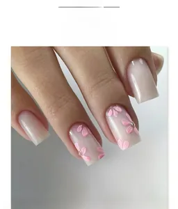Dettaglio di unghie finte quadrate con sfumatura rosa, fiori 3D e decori in strass