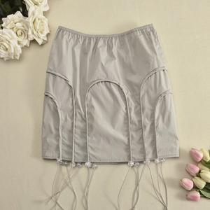 Détail de la mini-jupe taille basse en tissu satiné avec perles et franges décoratives