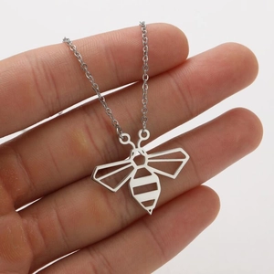 Detail of silver hollow bee pendant necklace held by hand showing geometric design