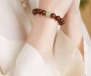 Detail of wooden prayer beads featuring a green jade bead on a silk sleeve wrist