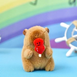 Close-up of a cute brown plush capybara keychain holding a small smiling red strawberry toy