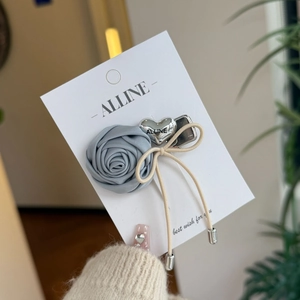 Detailed shot of a blue satin rose hair clip with silver heart charm and cream bow tie