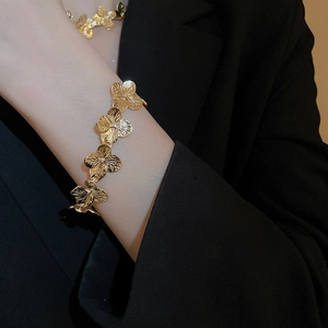 Close-up of a gold metal flower link bracelet with four-petal floral patterns on a wrist