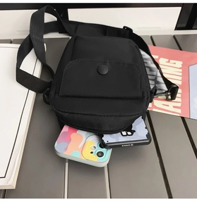 Compact black nylon crossbody bag showing storage capacity for two smartphones