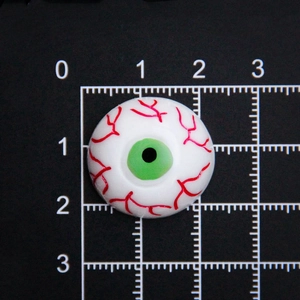 Accessoire œil en résine de 2cm pour Halloween avec iris vert et veines rouges sur règle