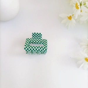 Close-up of small green and white checkered acrylic hair claw clip on a white table