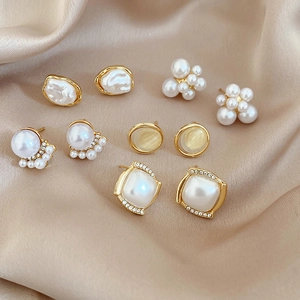 Detailed macro view of gold plated pearl earrings collection on silk fabric background