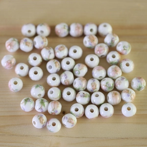 Macro shot of white ceramic beads with pink floral patterns on natural wood surface