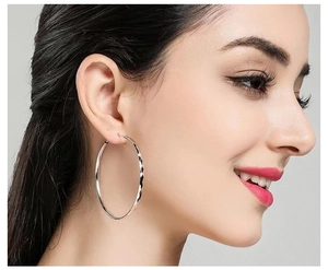 Detail view of large silver hoop earrings with diamond-cut faceted texture on model