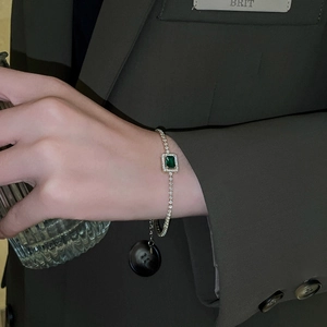 Close-up of emerald-cut green stone tennis bracelet worn with stylish blazer outfit