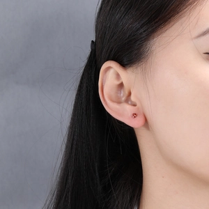 Close-up of a s925 silver stud earring with a round red zircon worn by a model