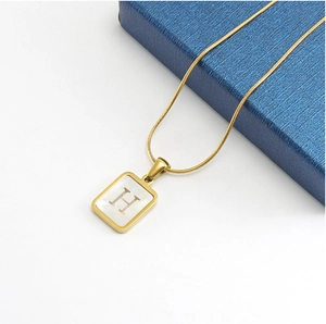 Close-up of gold-plated pendant with white mother of pearl inlay and H initial