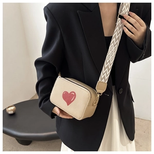 Close-up of beige crossbody bag with red heart pattern and geometric woven wide strap