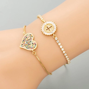 Detail view of two gold layered bracelets featuring heart charm and zircon cross on wrist