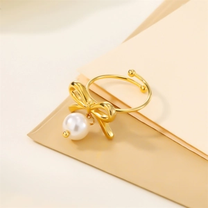 Detail of 18k gold butterfly bow ring with a white pearl charm on cream background