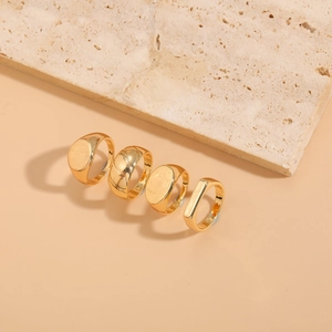 Detailed view of four minimalist 14K gold plated geometric rings on beige stone