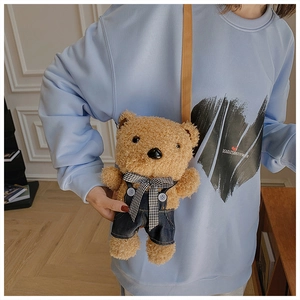 Detailed view of a brown plush bear crossbody bag wearing blue denim overalls and a bow tie