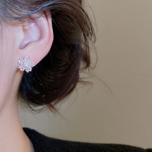 Close-up of elegant snowflake stud earrings with pink and clear zircons on model ear