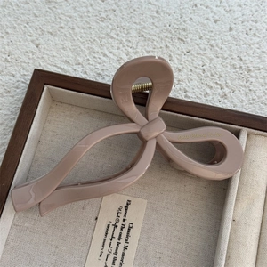 Close-up of beige glossy bow hair claw clip with golden Only Belong To You text